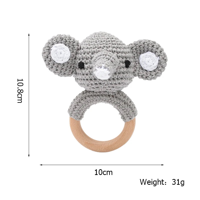 Crocheted elephant rattle with a wooden ring, measuring 10.8cm by 10cm and weighing 31g. The elephant has plush ears and a trunk, ideal for babies to hold and play with.