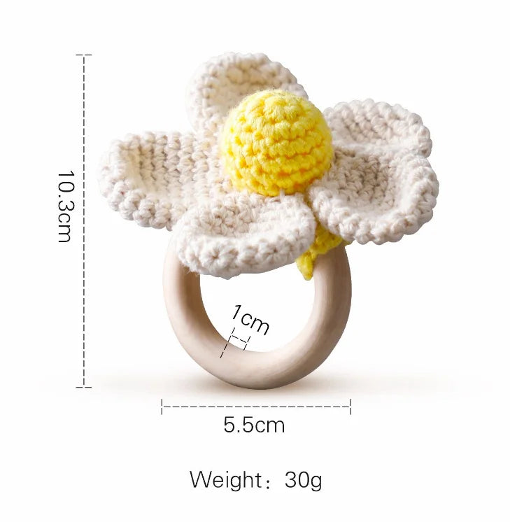 Crochet daisy teether with yellow center and white petals, attached to a wooden ring. Dimensions: 10.3cm high, 5.5cm wide, 1cm thick; weighs 30g.
