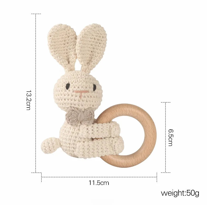 Crocheted bunny ring rattle with a wooden handle. The bunny has long ears, a small tail, and a bow tie. Dimensions are 13.2cm x 11.5cm x 6.5cm, and it weighs 50 grams.