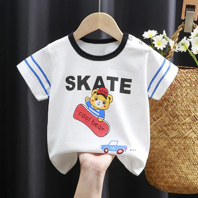 White baby T-shirt with black neckline and blue-striped sleeves featuring a cartoon bear on a skateboard. "SKATE" and "cool bear" are printed on the front. Hangs on a wooden hanger.