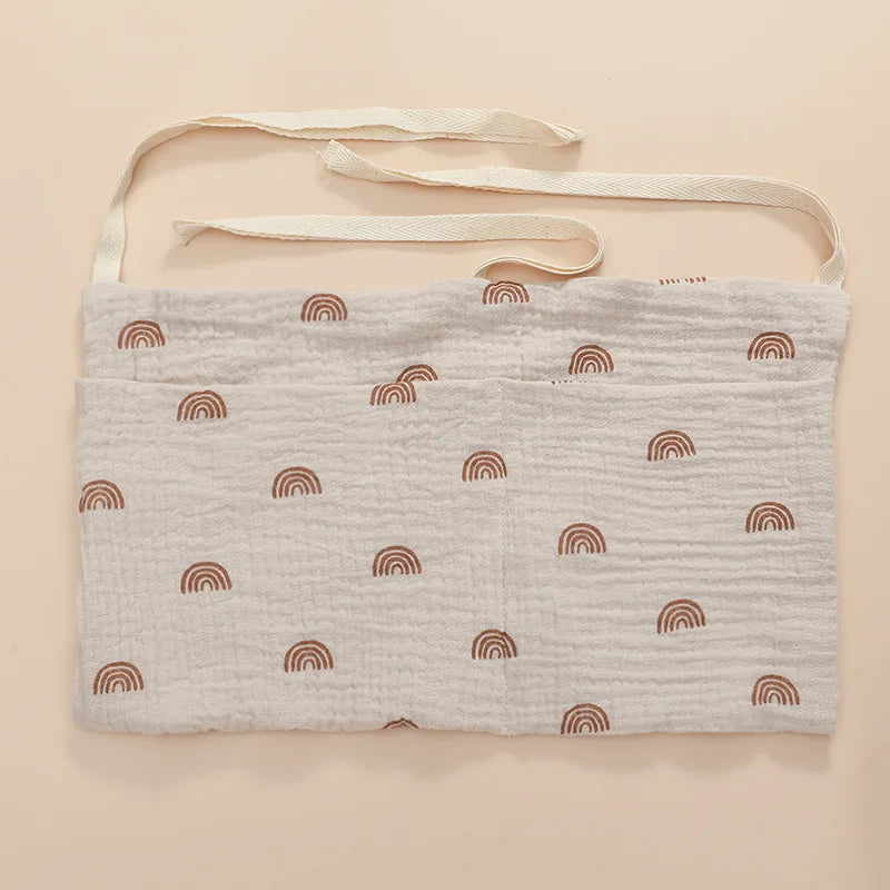 White muslin pouch with brown rainbow patterns, featuring two long beige straps for tying. The fabric has a crinkled texture.