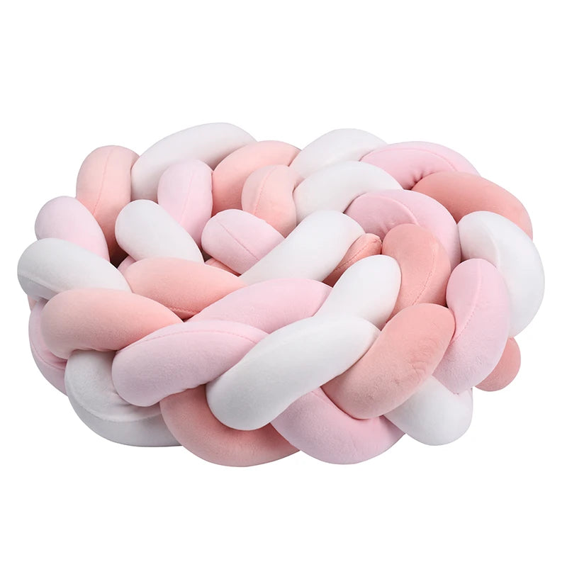 A plush, round throw pillow featuring a braided design in soft hues of pink, white, and peach, creating a cozy and inviting appearance.