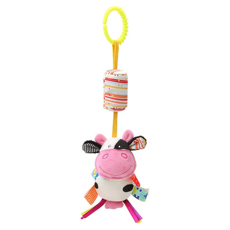 Colorful plush cow toy with a pink face, black and white ears, and colorful ribbon legs, hanging from a yellow plastic loop. Includes a striped padded section above the cow.