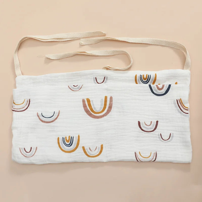 White fabric with colorful, semi-circular rainbow patterns and beige ties, laid flat on a solid peach background.
