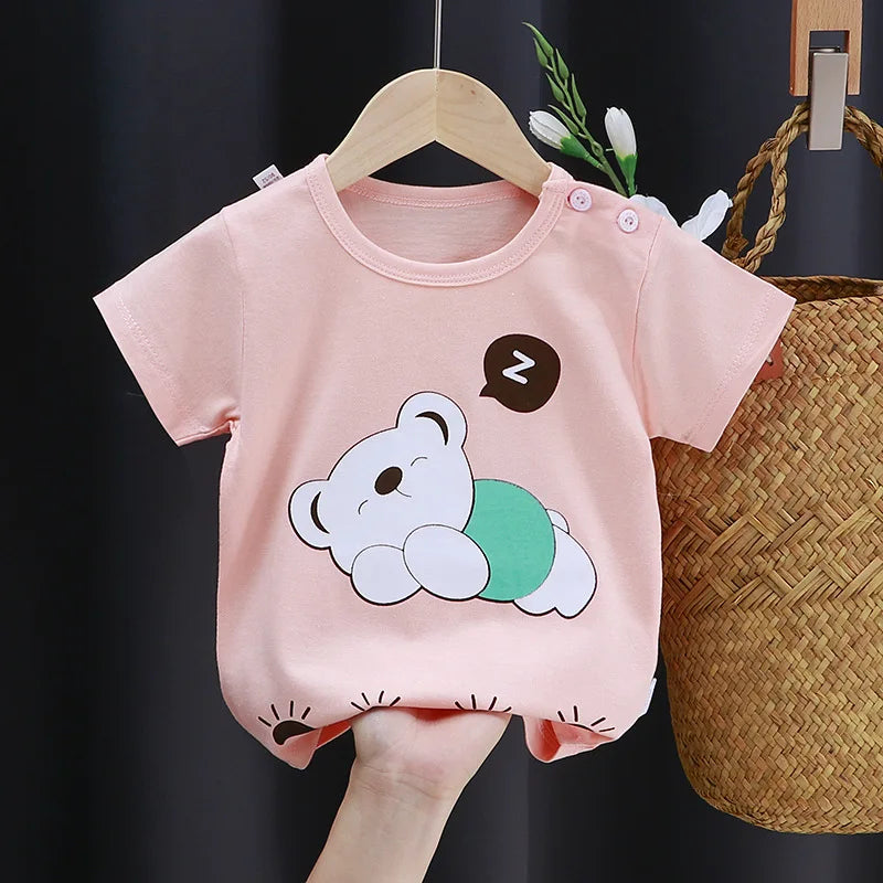 Pink baby shirt with a cute sleeping bear graphic and a "Z" bubble, hung on a wooden hanger. Basket and flowers in the background.