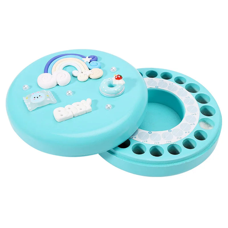 Round blue object with a lid featuring a rainbow, clouds, "baby" text, and small decorative items. The base has holes arranged in a circle, resembling a jewelry or toy organizer.