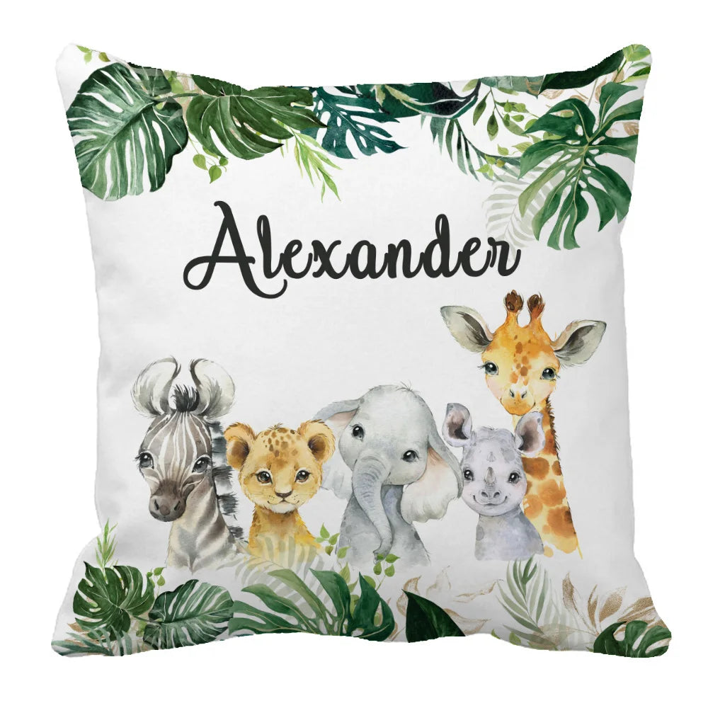 A decorative pillow featuring the name "Alexander" surrounded by watercolor jungle foliage and cartoon baby animals: a zebra, lion, elephant, rhino, and giraffe.
