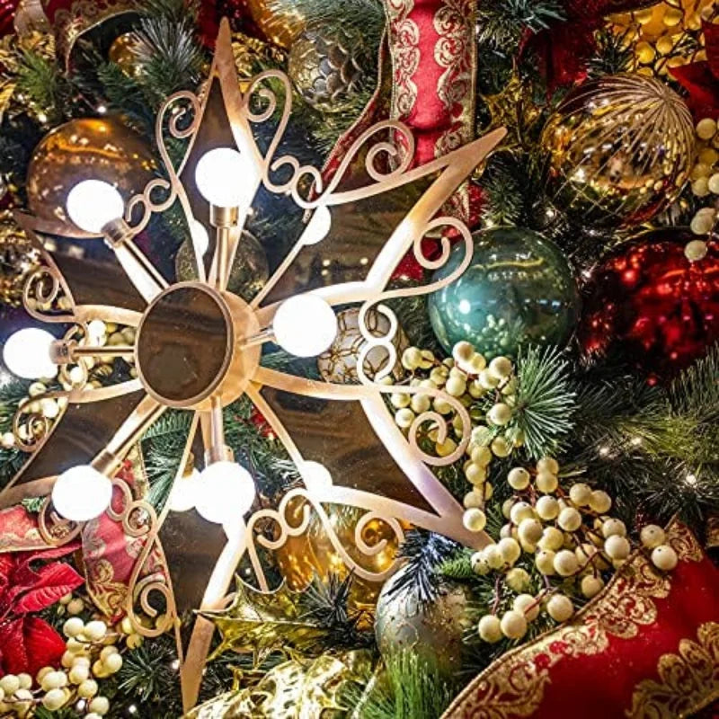 A festive holiday display featuring a gold ornamental star with glowing lights, surrounded by red and gold ribbons, baubles, pinecones, and lush evergreen branches.