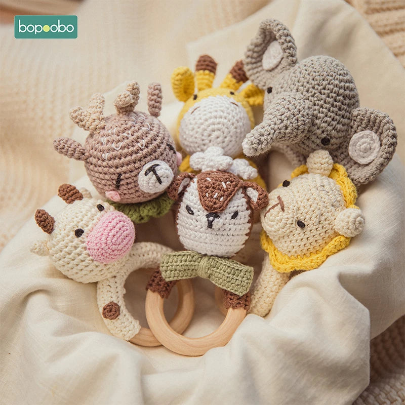 Handmade crochet rattles shaped like animals, including a deer, cow, bear, giraffe, lion, and elephant, arranged on a soft beige fabric.
