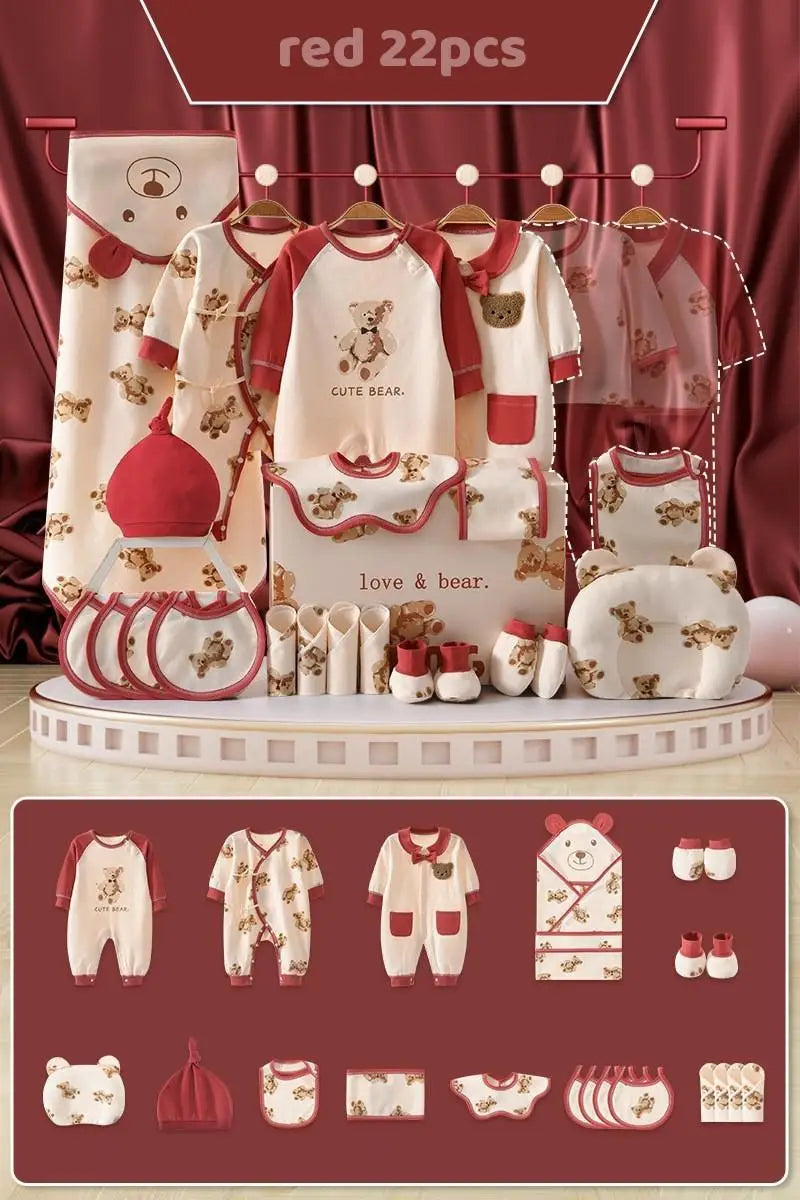 Red and cream 22-piece baby clothing set featuring bear designs. Includes pajamas, hats, bibs, rompers, a blanket, and shoes. Displayed on a stage with a red curtain backdrop.