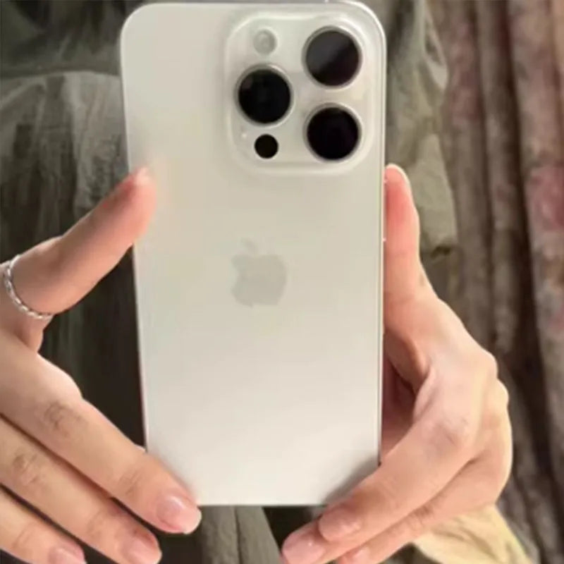 A person is holding a white smartphone with a large camera module featuring three lenses and an Apple logo. The device is being held with two hands in front of a blurred background.