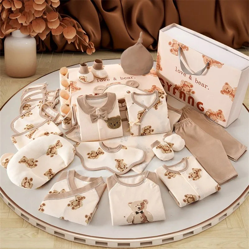 Baby clothing set with teddy bear patterns, including onesies, bibs, mittens, and hats. Arranged neatly, accompanied by a decorative paper bag and surrounded by warm decor.