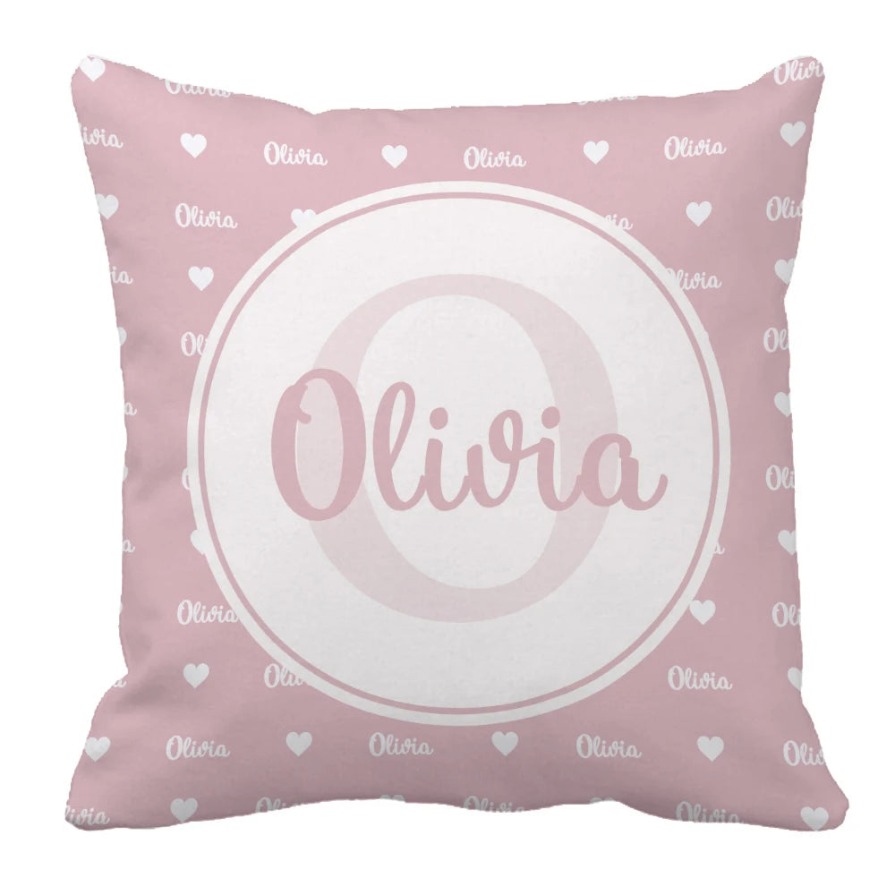 Pink throw pillow with the name "Olivia" in white script, surrounded by a circle. The background is patterned with smaller "Olivia" text and white hearts.