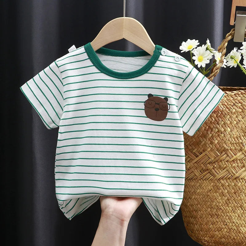 Striped baby t-shirt with green trim and bear face design on chest, held by a hand. Basket with daisies in background, against a dark curtain backdrop.