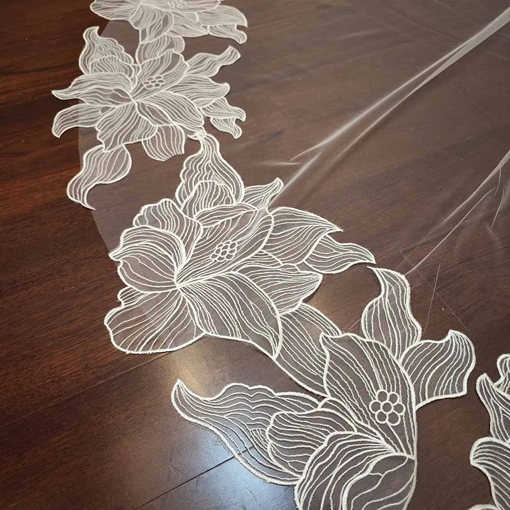Elegant floral lace fabric with white embroidered flowers on a dark wooden surface, showcasing intricate details and delicate patterns.