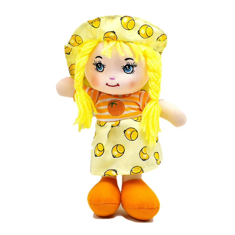 A colorful rag doll with bright yellow hair, wearing a matching hat and dress with lemon patterns, striped orange shirt, and orange shoes, smiles cheerfully.