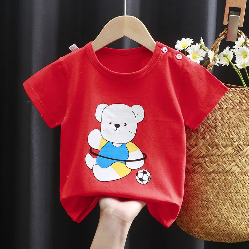 Red toddler t-shirt with a playful teddy bear print wearing a blue and yellow outfit, holding a hula hoop, and next to a soccer ball. It hangs on a wooden hanger.