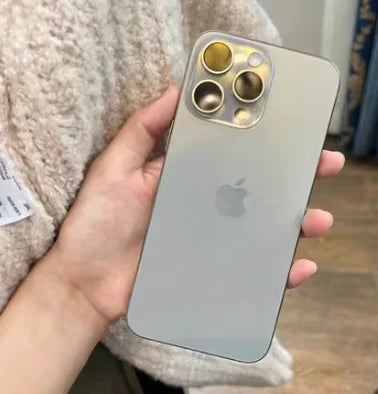 A hand holding a sleek, silver smartphone with three large camera lenses on the back, resting against a textured, beige fabric. The iconic Apple logo is visible on the device.