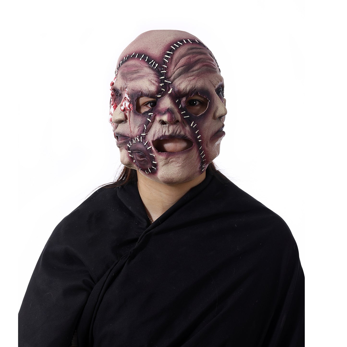Person in a black cloak wearing a grotesque, stitched-together horror mask with multiple faces and visible stitches, set against a white background.