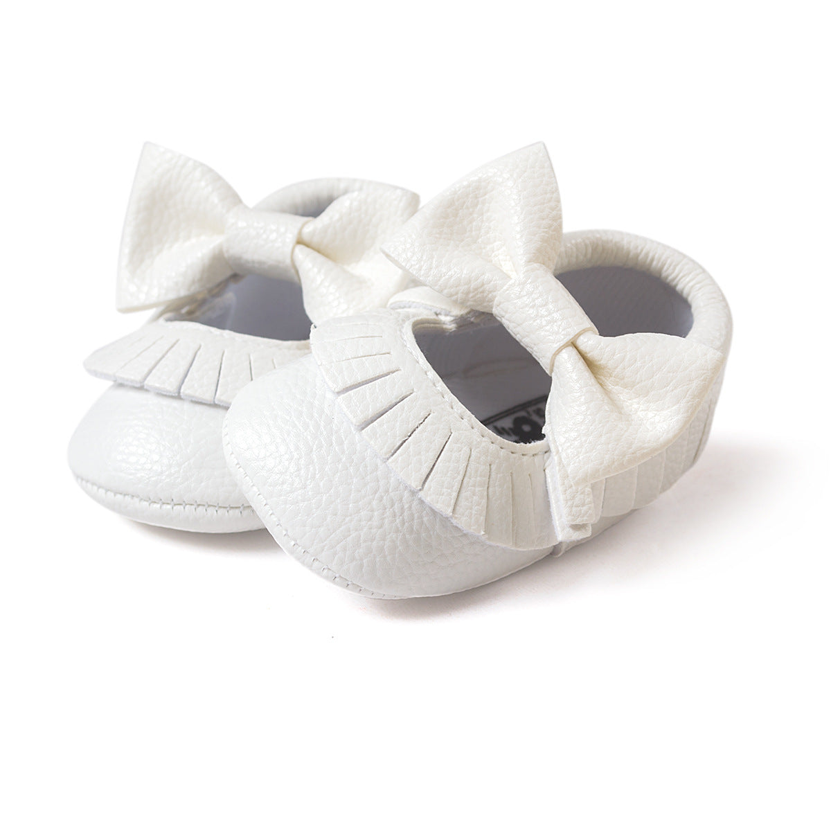 White baby shoes with textured surface, featuring decorative fringe and large matching bows on the front. The shoes have a soft, rounded design suitable for infants.