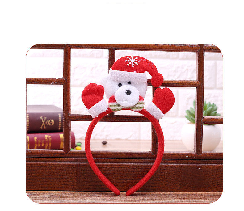 Red headband with a cute polar bear wearing a Santa hat and mittens. Bear has a green bow tie and is displayed on a wooden shelf with books and a small plant in the background.