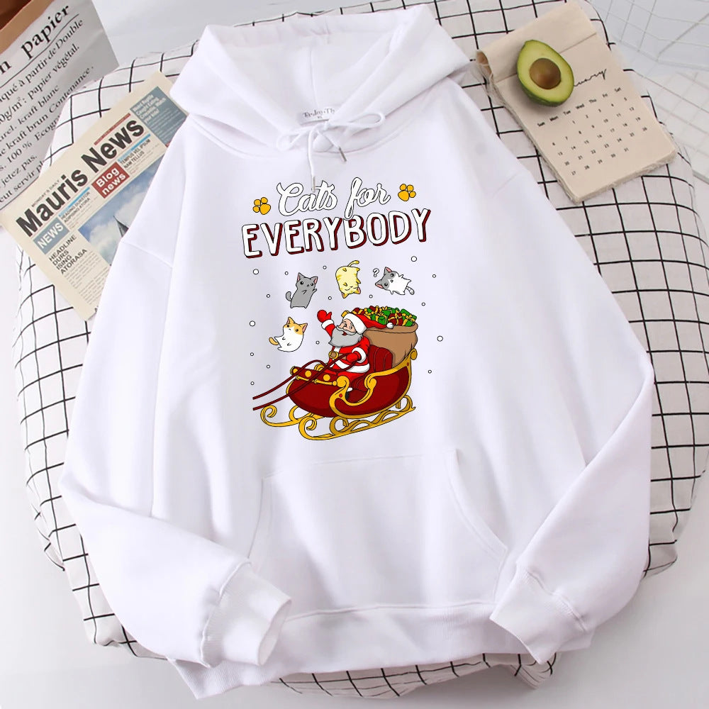 White hoodie featuring Santa in a red sleigh with cats and text "Cats for Everybody." Surrounded by a newspaper, avocado, and calendar on a checked cloth.