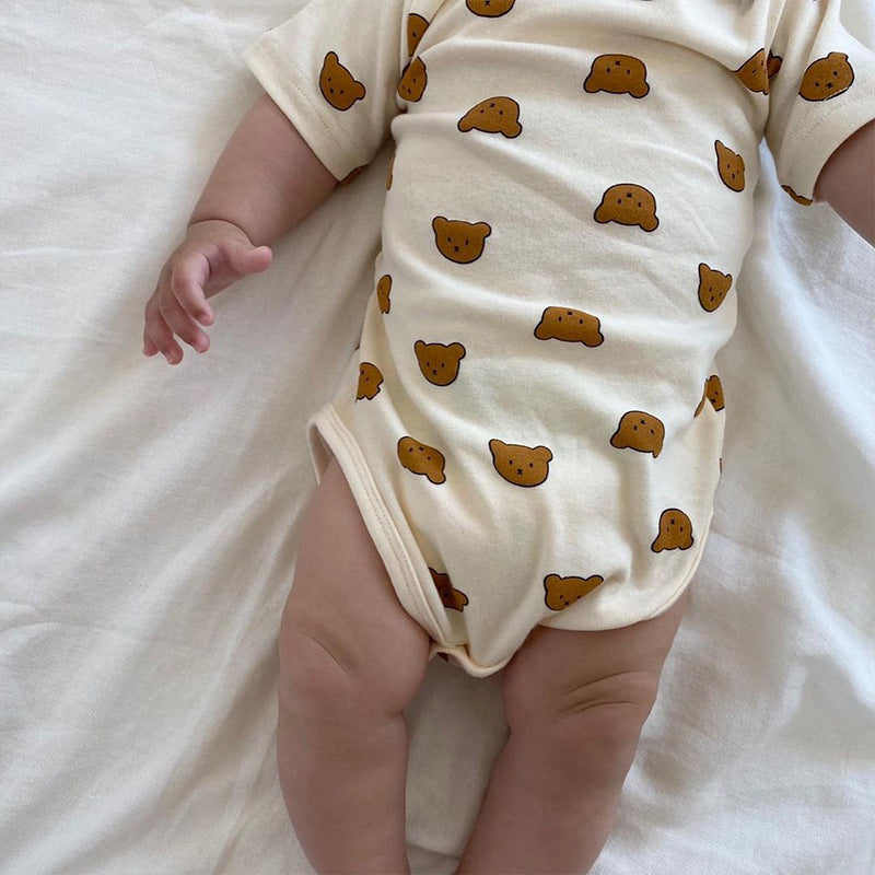 Baby wearing a cream onesie with brown bear faces lying on a white sheet. Only the torso and legs are visible, showcasing the cute bear pattern.