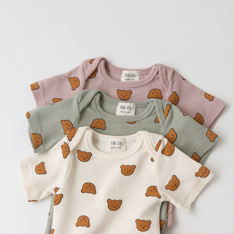 Three baby onesies in cream, green, and mauve with brown teddy bear faces neatly stacked. Each is labeled "BEBE LIEBE" and displayed on a white background.