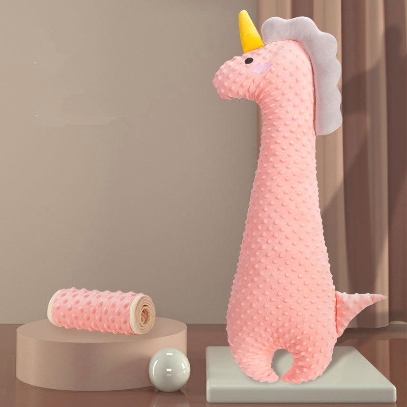 Pink plush unicorn toy with textured bumps, featuring a yellow horn and white mane, stands upright. A matching rolled towel and white sphere are displayed nearby.