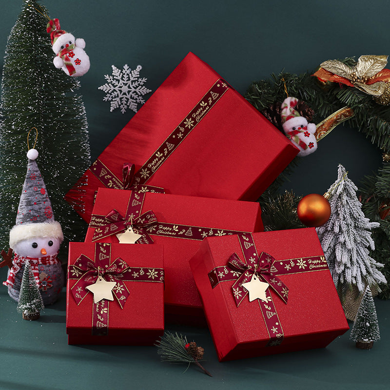 Red gift boxes with star tags and festive ribbons are surrounded by mini Christmas trees, a wreath, and snowman decorations on a green background.