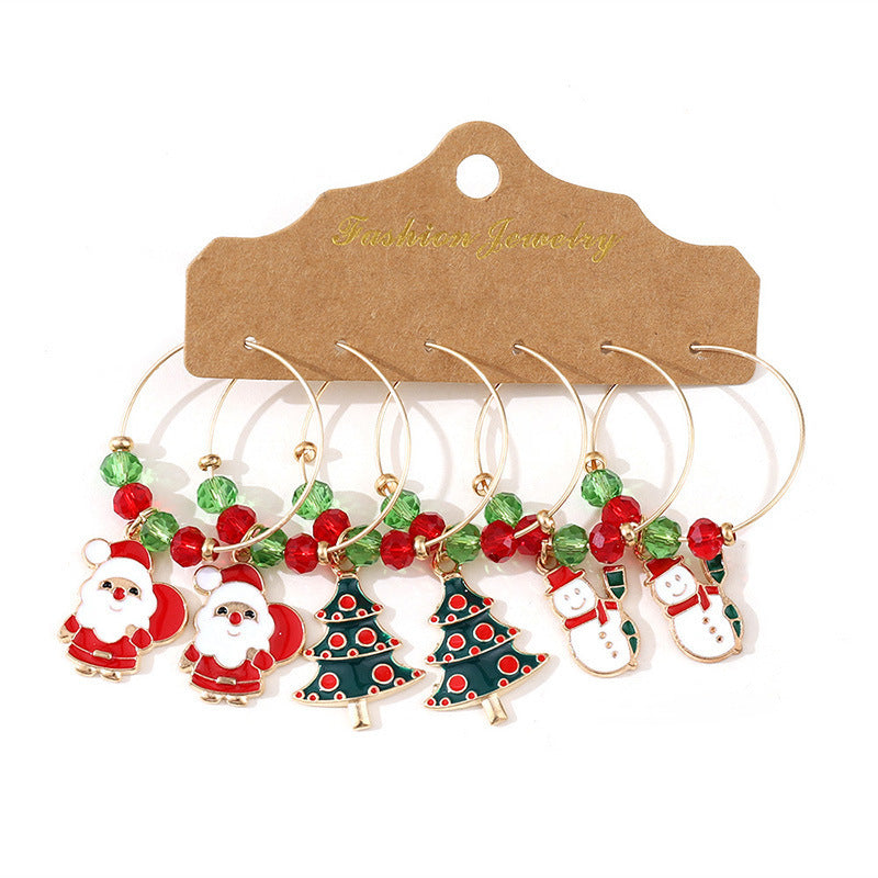 Set of six festive wine glass charms featuring Santa, Christmas trees, and snowmen. Adorned with red and green beads, these charms are attached to gold-tone hoops.