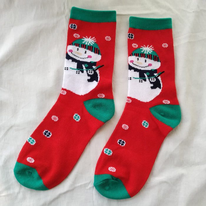 Red socks featuring a smiling snowman design with a green beanie and scarf. The socks have green accents on the toes and cuffs, with colorful snowflakes scattered around.