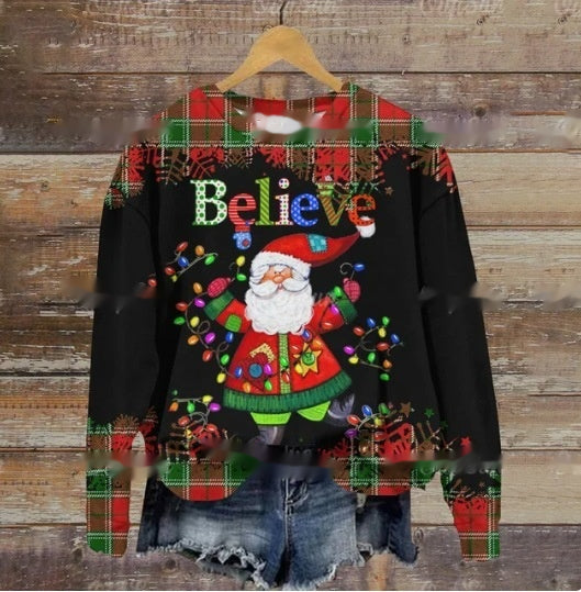 Festive sweater featuring Santa holding colorful lights with the word "Believe." Plaid accents on shoulders and sleeves. Paired with denim shorts on a wooden hanger.