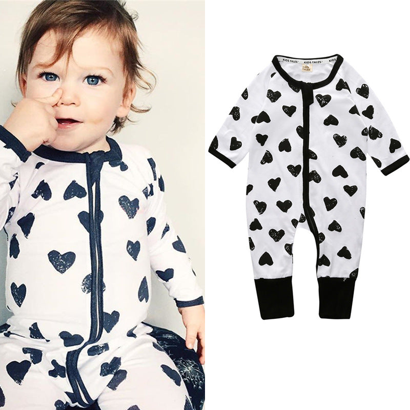 A toddler wearing a white onesie with black heart patterns and black trim. Next to the child is the same onesie displayed alone, highlighting its design.