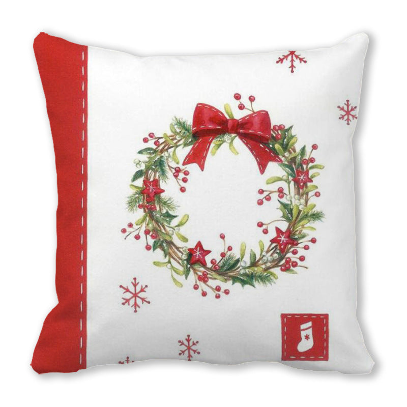 White cushion with red edges featuring a festive wreath with greenery, red berries, and a bow. Red stars and snowflakes are also part of the design.