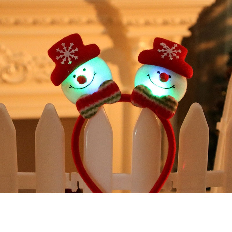 Festive headband with two glowing snowmen decorations wearing red hats and striped scarves, perched on a white fence in front of a blurred background.