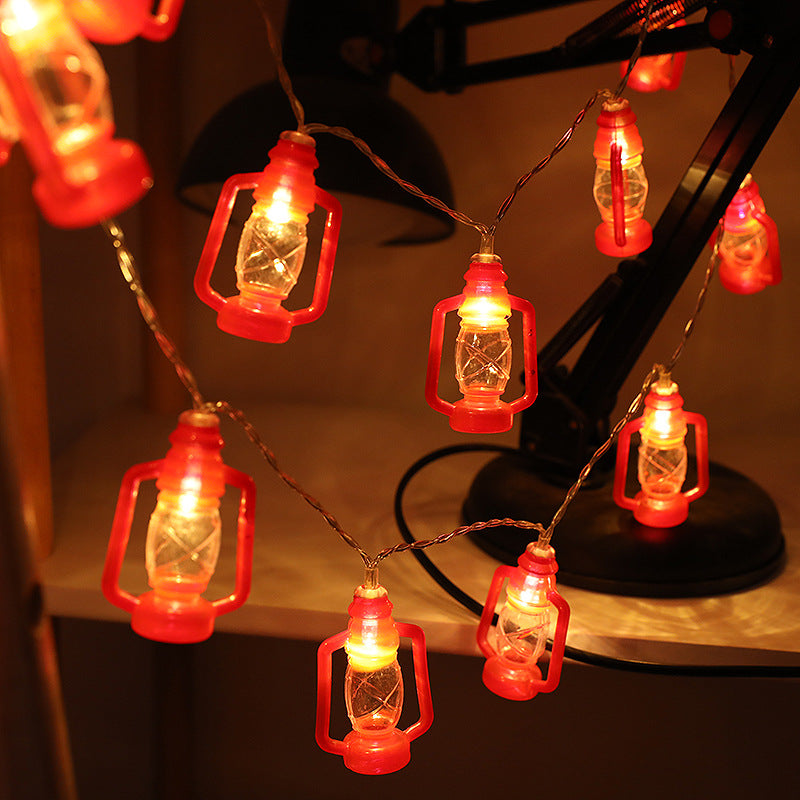 String lights designed like small red lanterns illuminate a cozy space, hanging near a black desk lamp, casting a warm, soft glow in the dimly lit room.