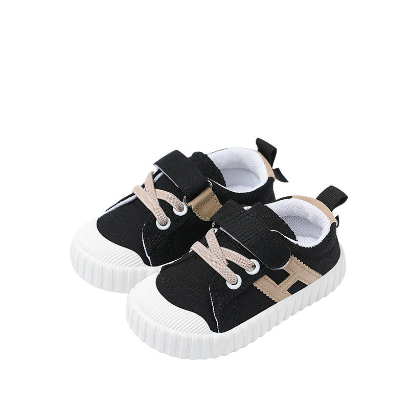 Black toddler shoes with white soles and beige laces, featuring Velcro straps. They have a textured design and back pull tabs for easy wearing.