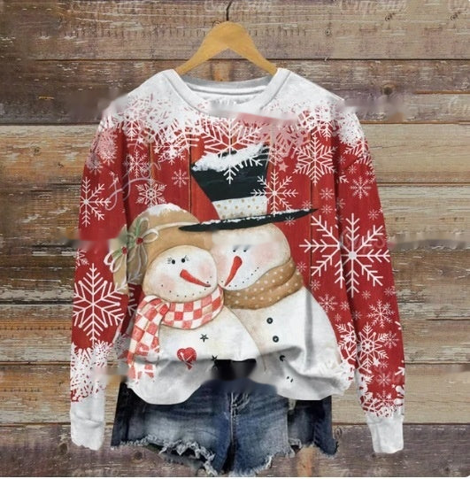 Red and white sweater with a snowmen couple design, wearing a scarf and top hat, surrounded by snowflakes, hung on a wooden hanger against a rustic wood background.