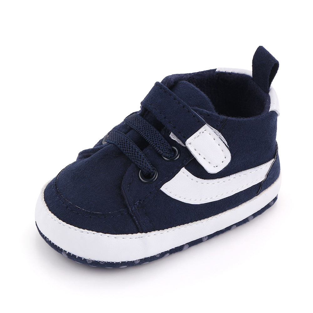 Navy blue baby sneaker with white accents, featuring a velcro strap, laces, and a loop at the back. The shoe has a soft sole with a dotted pattern for grip.