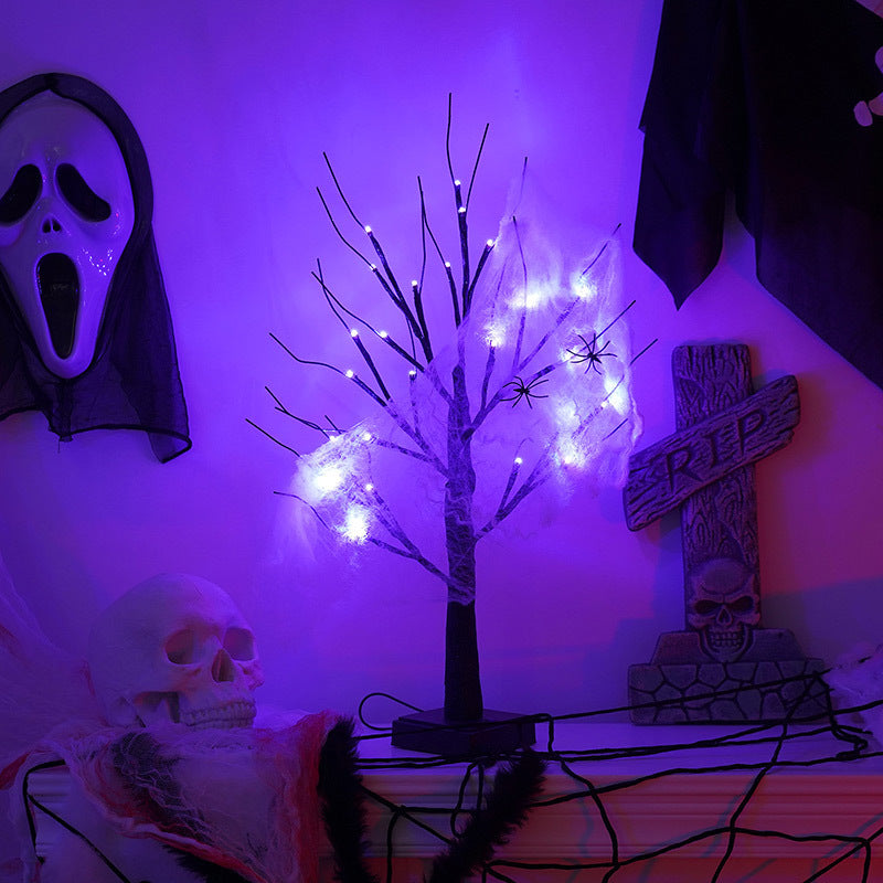 Halloween decorations with a lit tree, spider webs, spiders, skull, RIP gravestone, and a white mask on a purple-lit wall, enhancing the spooky ambiance.