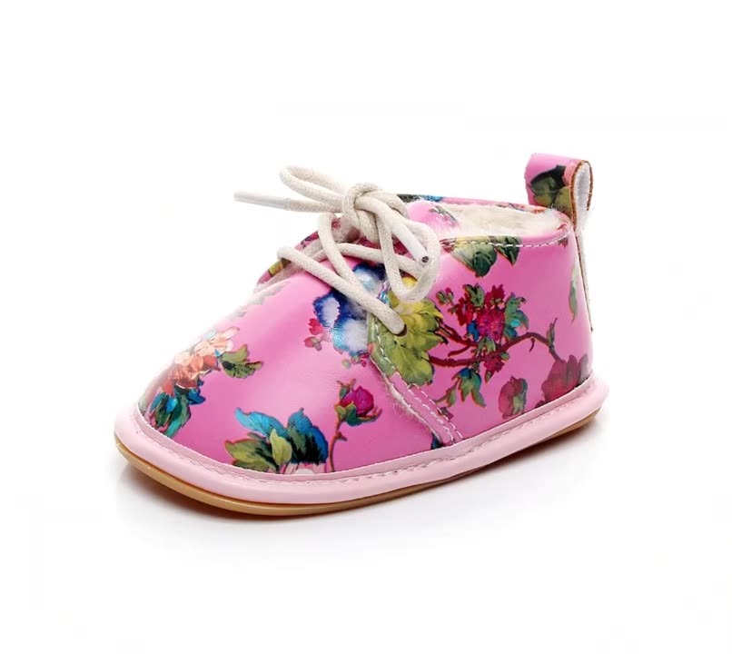 A pink baby shoe with a floral pattern, featuring white laces and a soft lining, designed for comfort and style.