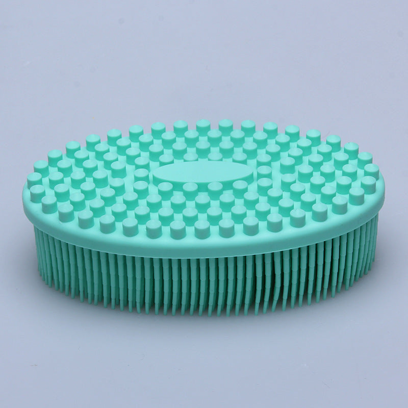 A turquoise silicone scalp brush with soft bristles and rounded tips is shown on a light gray background. The brush is oval-shaped with a textured, ergonomic grip.
