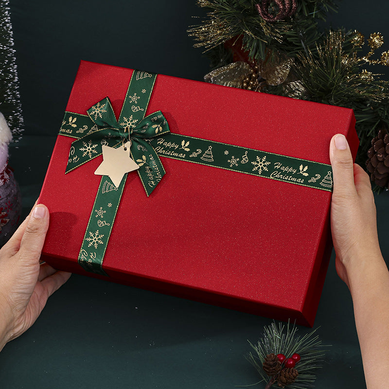 Hands holding a red gift box with a green ribbon and festive design, accented with a star-shaped tag. Holiday decorations visible in the background.