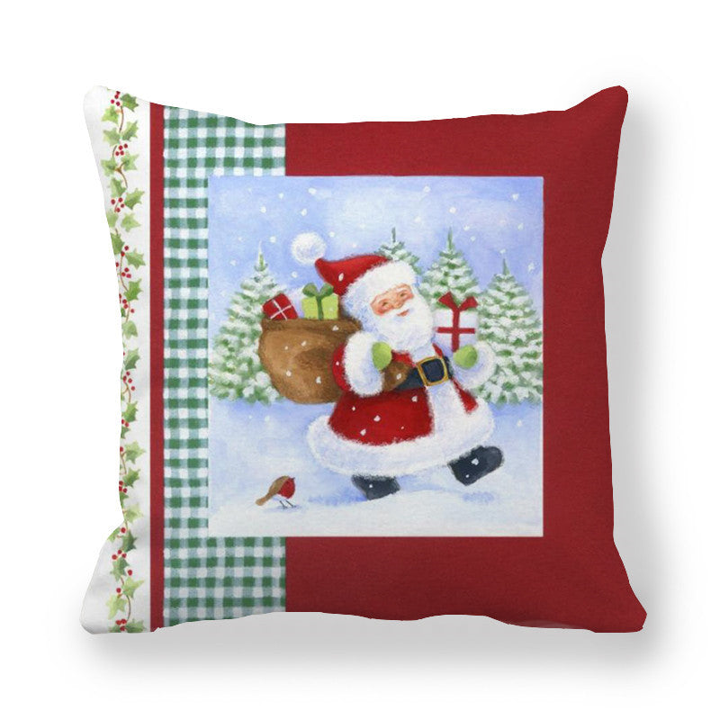 Festive pillow with Santa carrying gifts against a snowy forest backdrop, bordered by green gingham and holly patterns. Small red bird perches on snow.