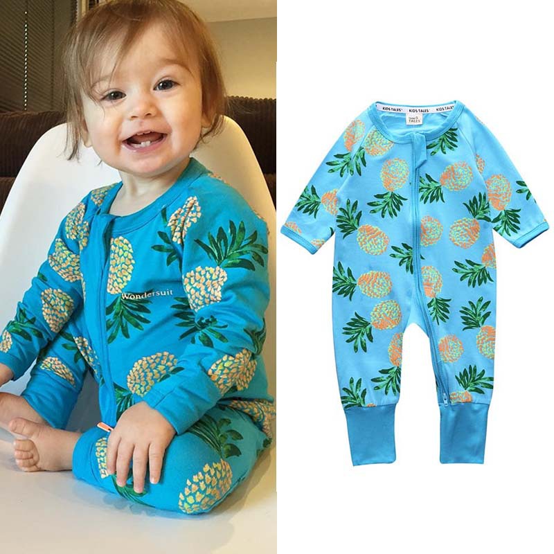 A smiling child wearing a blue onesie with a pineapple pattern sits in a chair. Beside them is a similar blue onesie with the same pineapple design displayed flat.