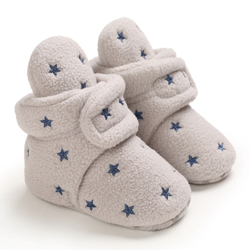 Cozy infant booties in soft gray fabric, decorated with small blue star patterns. The booties feature a wrap design for secure comfort, suitable for keeping little feet warm.