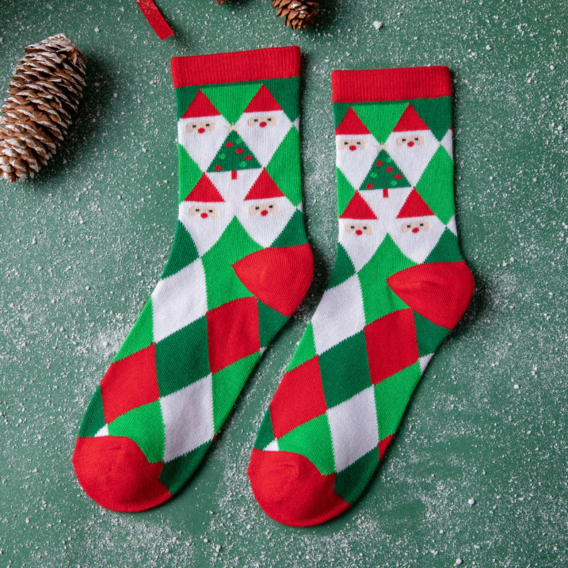 Festive socks with Santa and Christmas tree patterns in red, green, and white argyle design, surrounded by pinecones on a green, snowy surface.