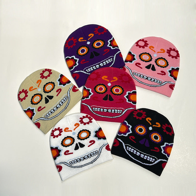 Five knit beanies with colorful sugar skull designs in purple, pink, tan, white, and black, featuring floral patterns and vibrant facial details, arranged on a light background.