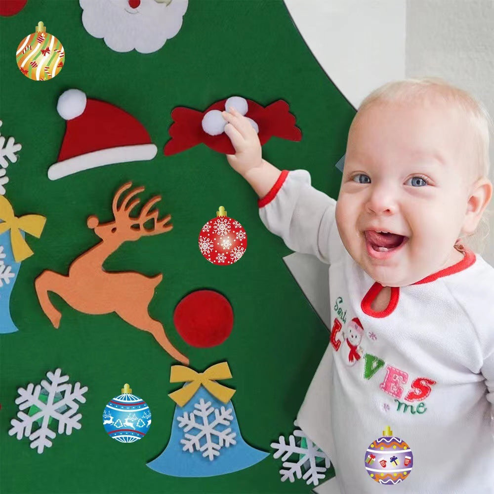 A smiling baby in festive pajamas reaches for a felt board with Christmas decorations, including a reindeer, Santa hat, snowflakes, and colorful ornaments.